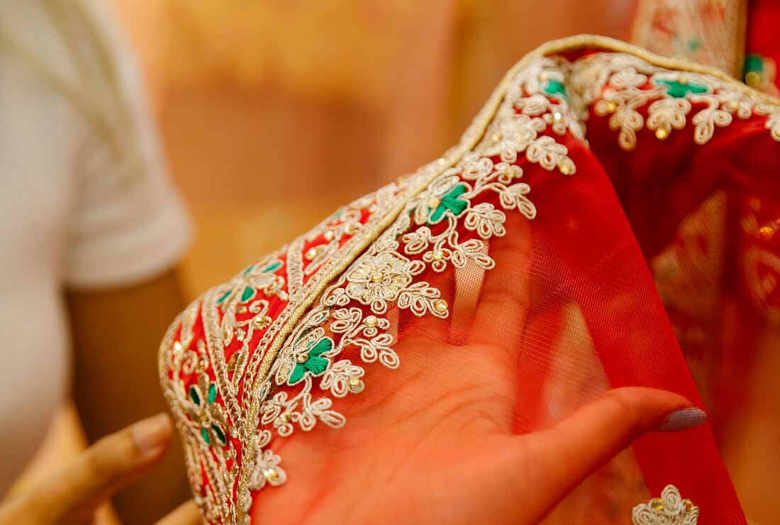 Close-up of hands over fine gold aari embroidery on red bridal fabric