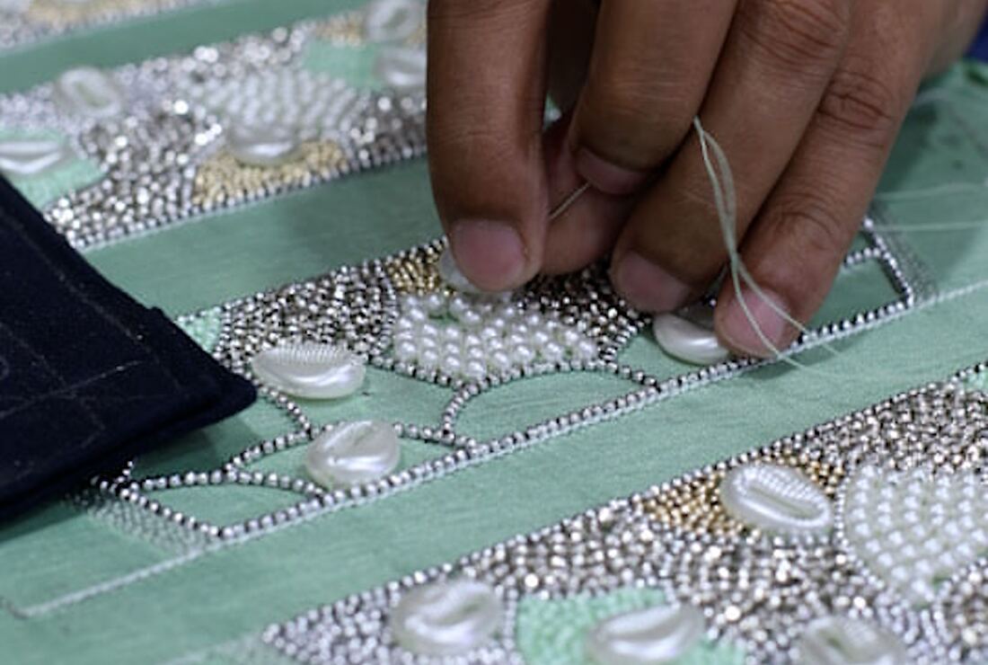 Artisan hand-stitching pearls and beads onto fabric on an embroidery frame